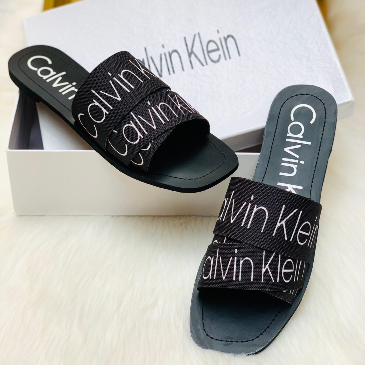 Black Calvin Klein women’s slide slipper placed on a white rug, stylish and comfortable design