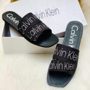 Black Calvin Klein women’s slide slipper placed on a white rug, stylish and comfortable design