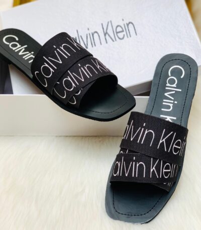 Black Calvin Klein women’s slide slipper placed on a white rug, stylish and comfortable design